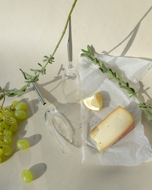 pointer wine glasses for champagne photographed next to cheese, lemon, white grapes and plants