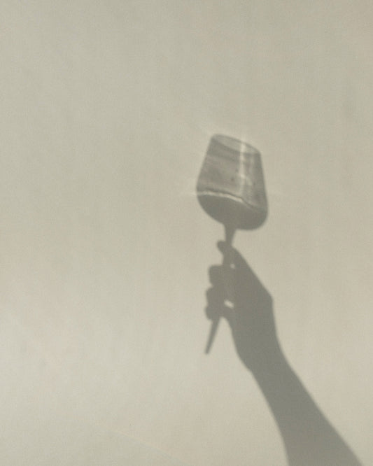 shadow of pointer wine glass held my a hand against a neutral background