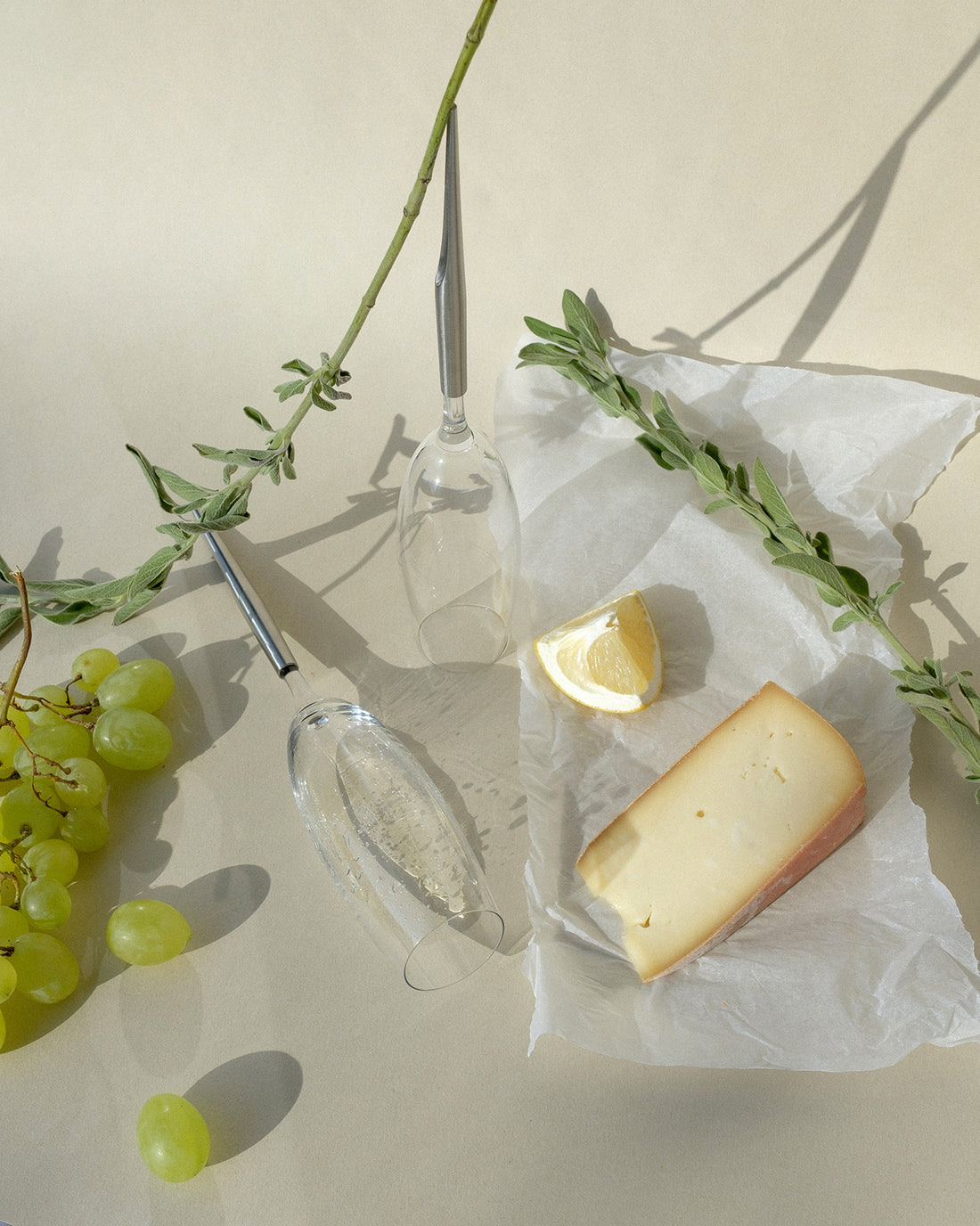 pointer wine glasses for champagne photographed next to cheese, lemon, white grapes and plants