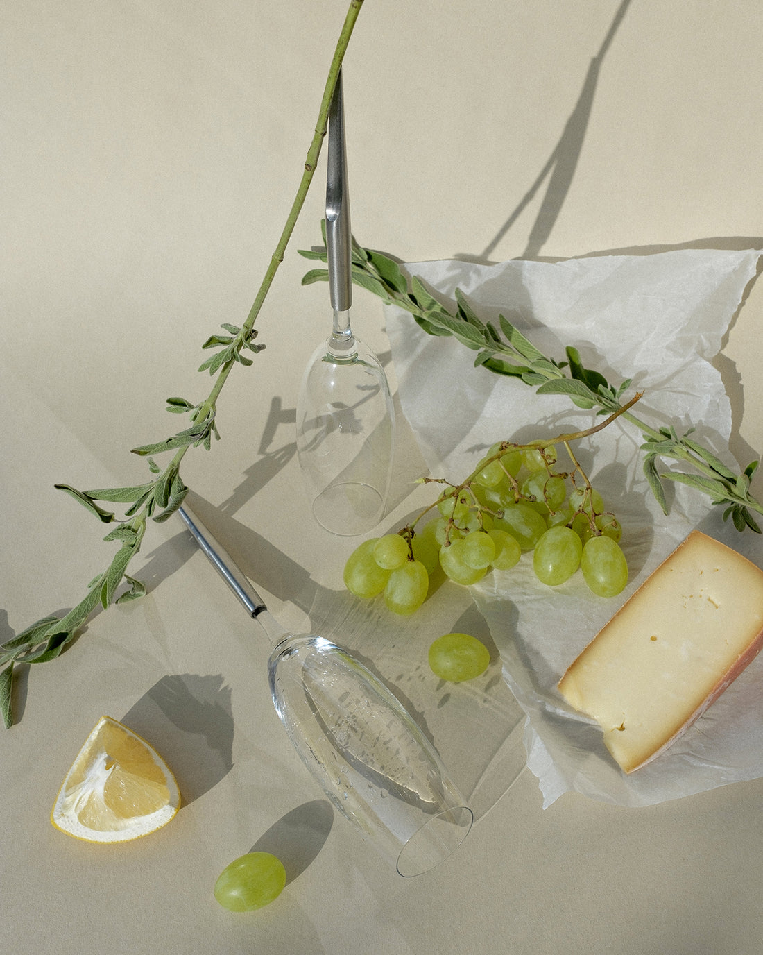 2 pointer wine glasses for champagne photographed on a beige background next to grapes, cheese, lemon and plants