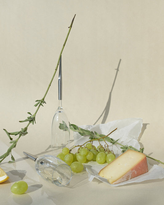 pointer champagne glasses next to cheese grapes and plants against a beige background