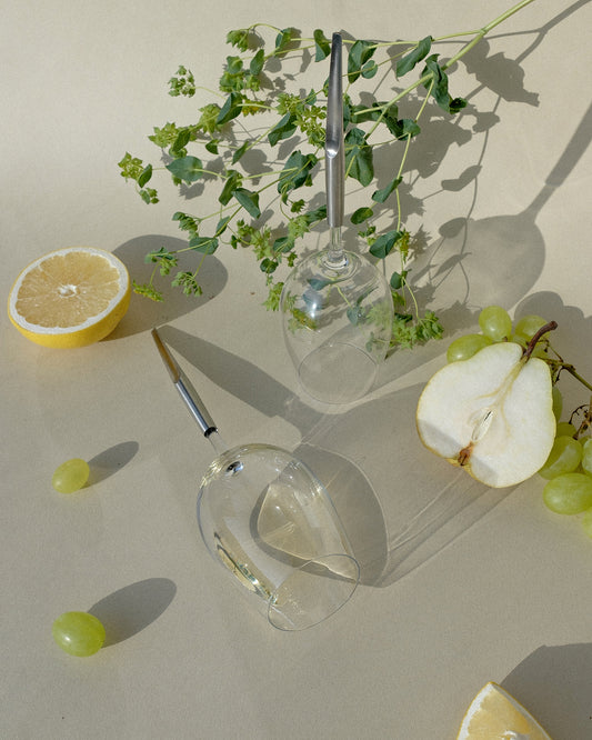 2 pointer wine glasses for white wine photographed on a beige background next to pears, lemons and plants