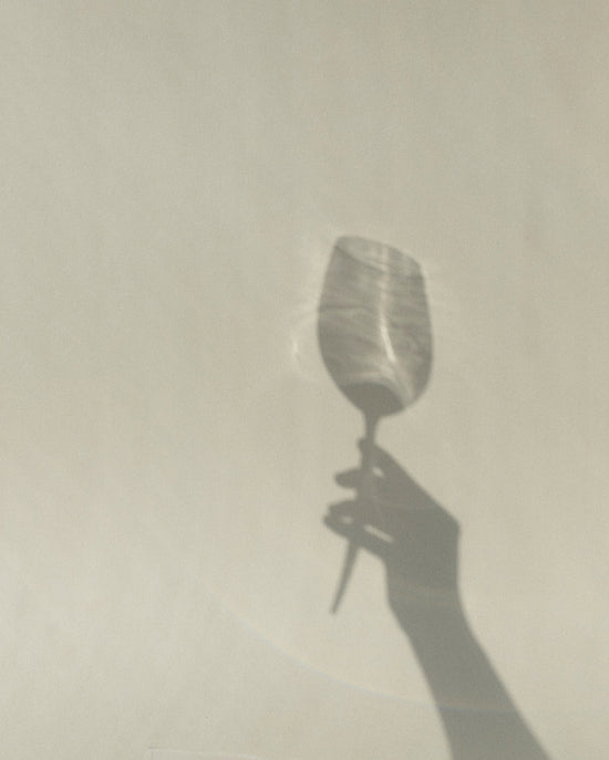 the shadow on a beige background of a picnic wine glass with metal pin and a hand holding it