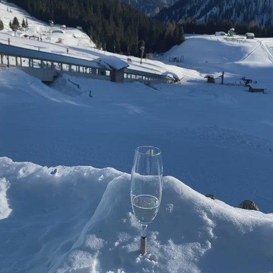 2 Pointer Champagne Glasses that are pinned in the snow with a metal component, overlooking the Austrian Alps on a sunny afternoon