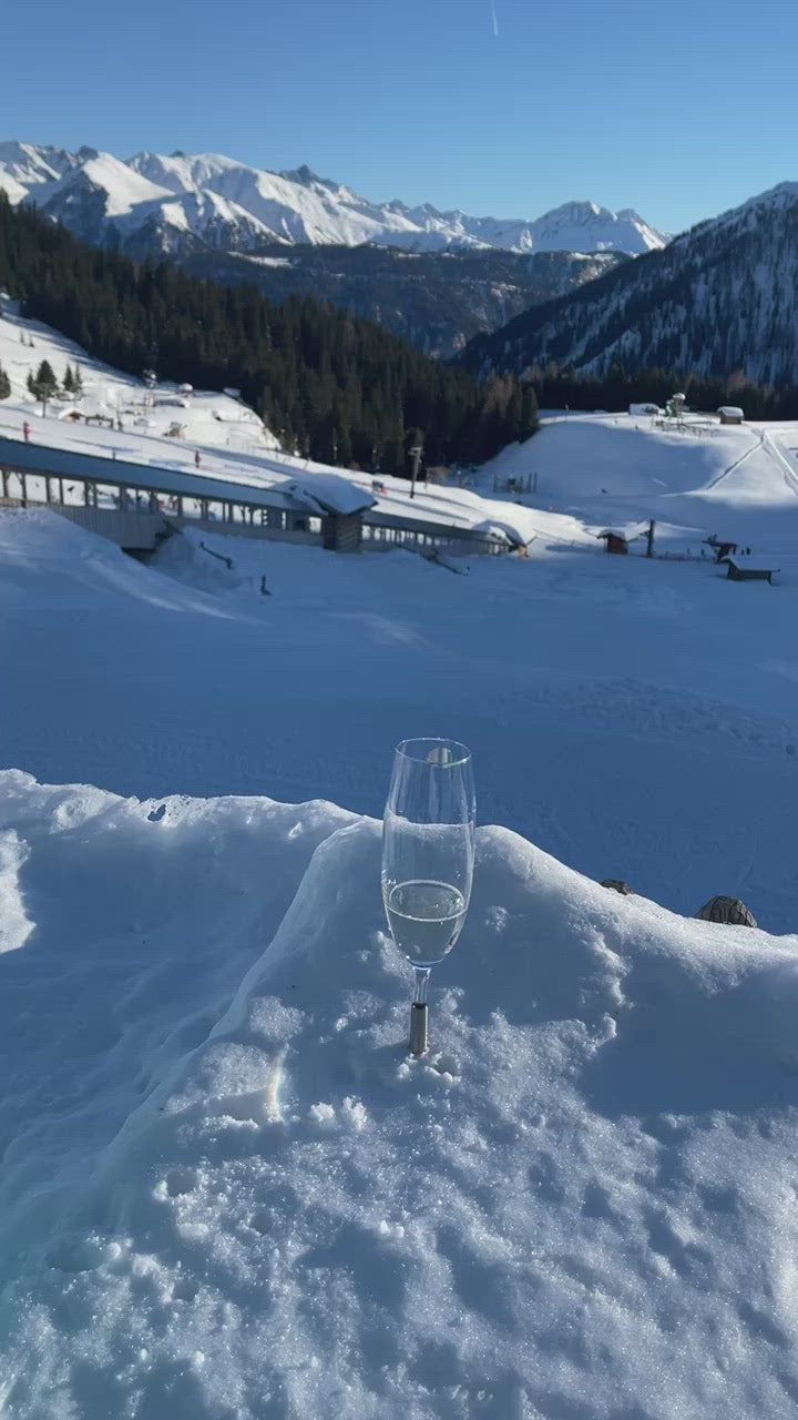 2 Pointer Champagne Glasses that are pinned in the snow with a metal component, overlooking the Austrian Alps on a sunny afternoon