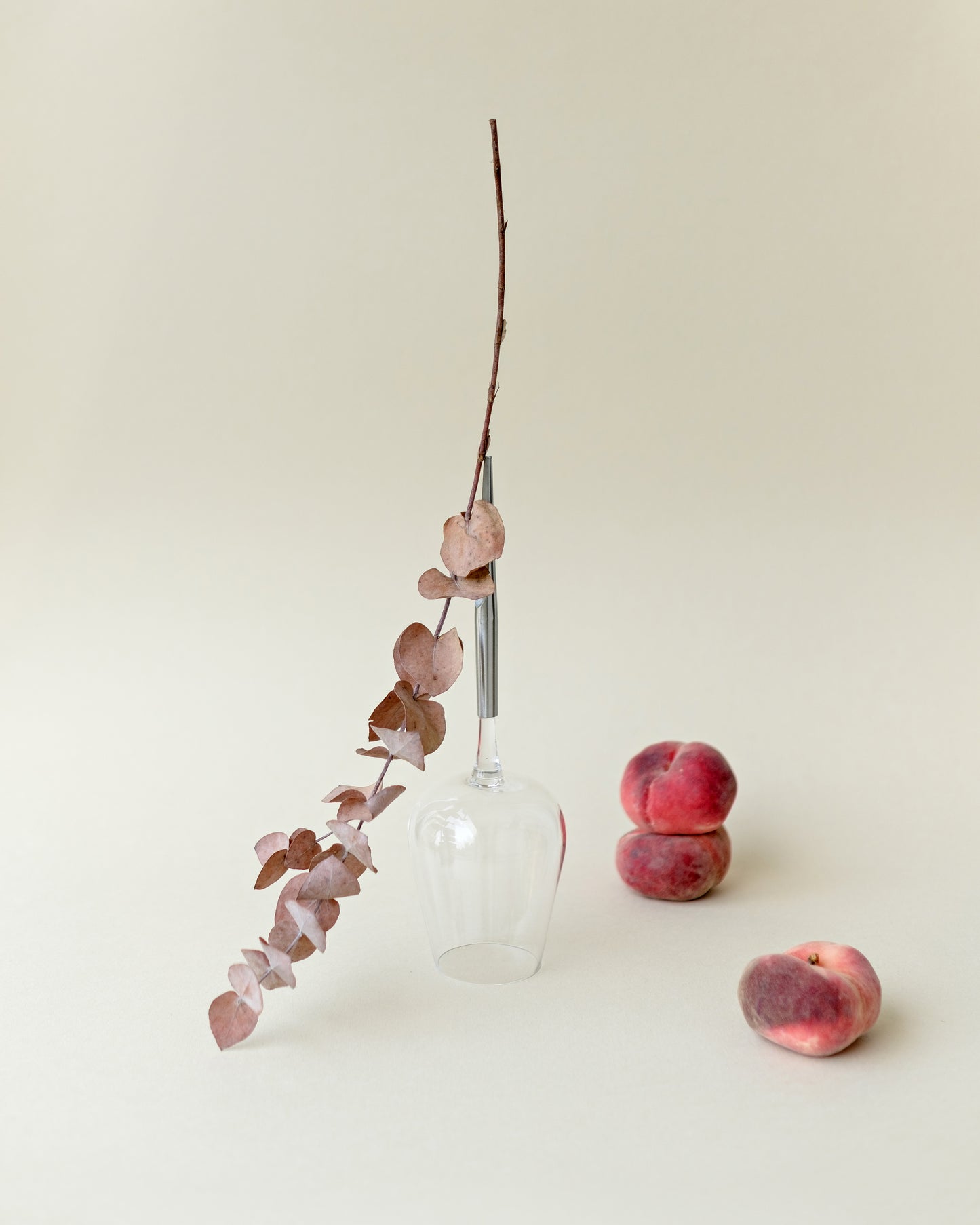 one wine glass for picnic with metal pin, placed upside down next to peaches and a plant branch