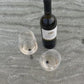 two beach wine glasses with a pointy metal pin placed in the sand and in the sea water next to a white wine bottle in Greek Island Paros