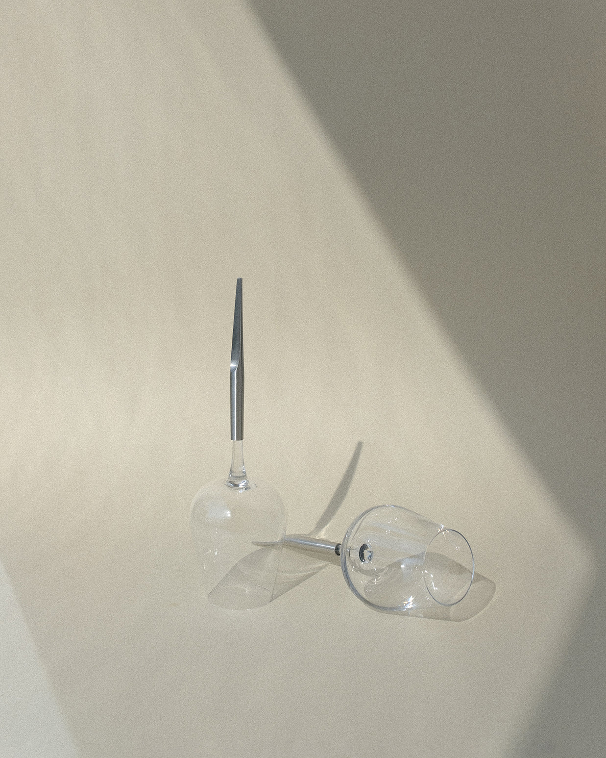 two wine glasses for picnic with metal pin, one upside down and one next to it laying horizontally, with shadows on the background