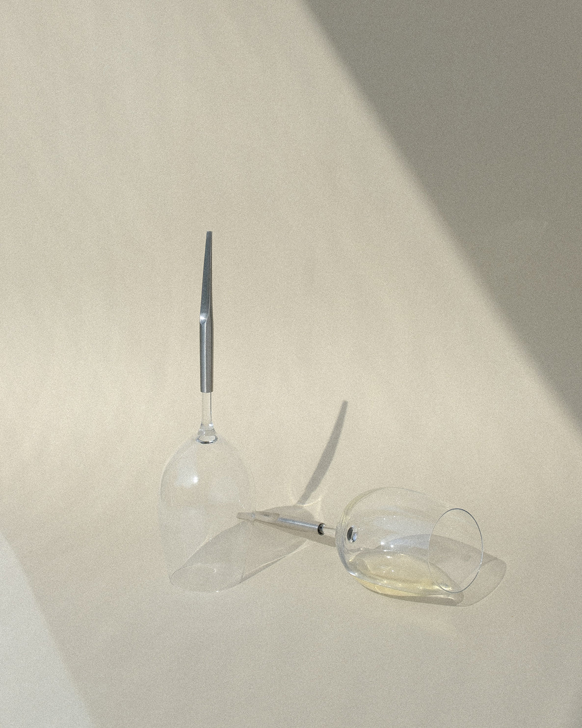 2 pointer wine glasses for white wine, made of crystal and with metal pins, placed next to each other on a table, one upside down and one half full, placed horizontally