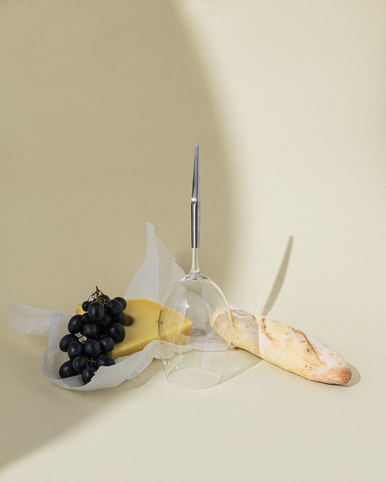 red wine glass for picnic with metal pin, placed upside down next to baguette, grape and cheese