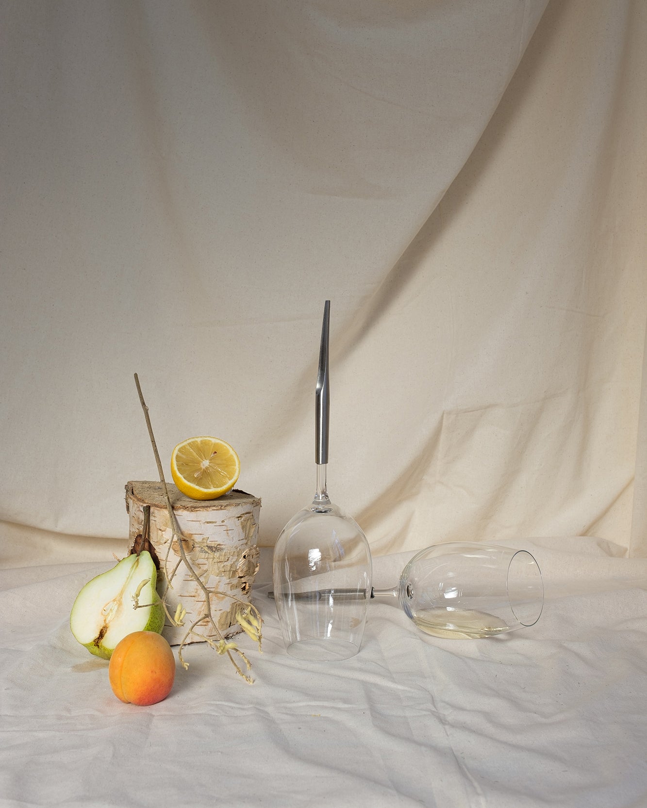 2 picnic wine glasses for white wine on a table cloth next to an apricot, half a pear and half a lemon; one picnic glass is upside down, the other one is horizontal and half full of wine