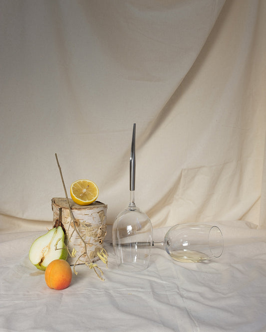 2 picnic wine glasses for white wine on a table cloth next to an apricot, half a pear and half a lemon; one picnic glass is upside down, the other one is horizontal and half full of wine