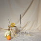 2 picnic wine glasses for white wine on a table cloth next to an apricot, half a pear and half a lemon; one picnic glass is upside down, the other one is horizontal and half full of wine