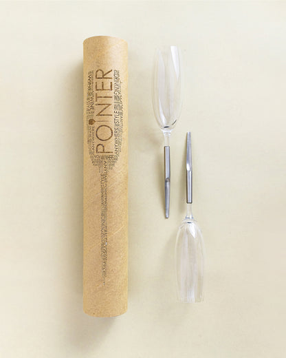 2 Pointer Crystal Champagne Glasses with metal Pin, laying parallel next to cardboard packaging