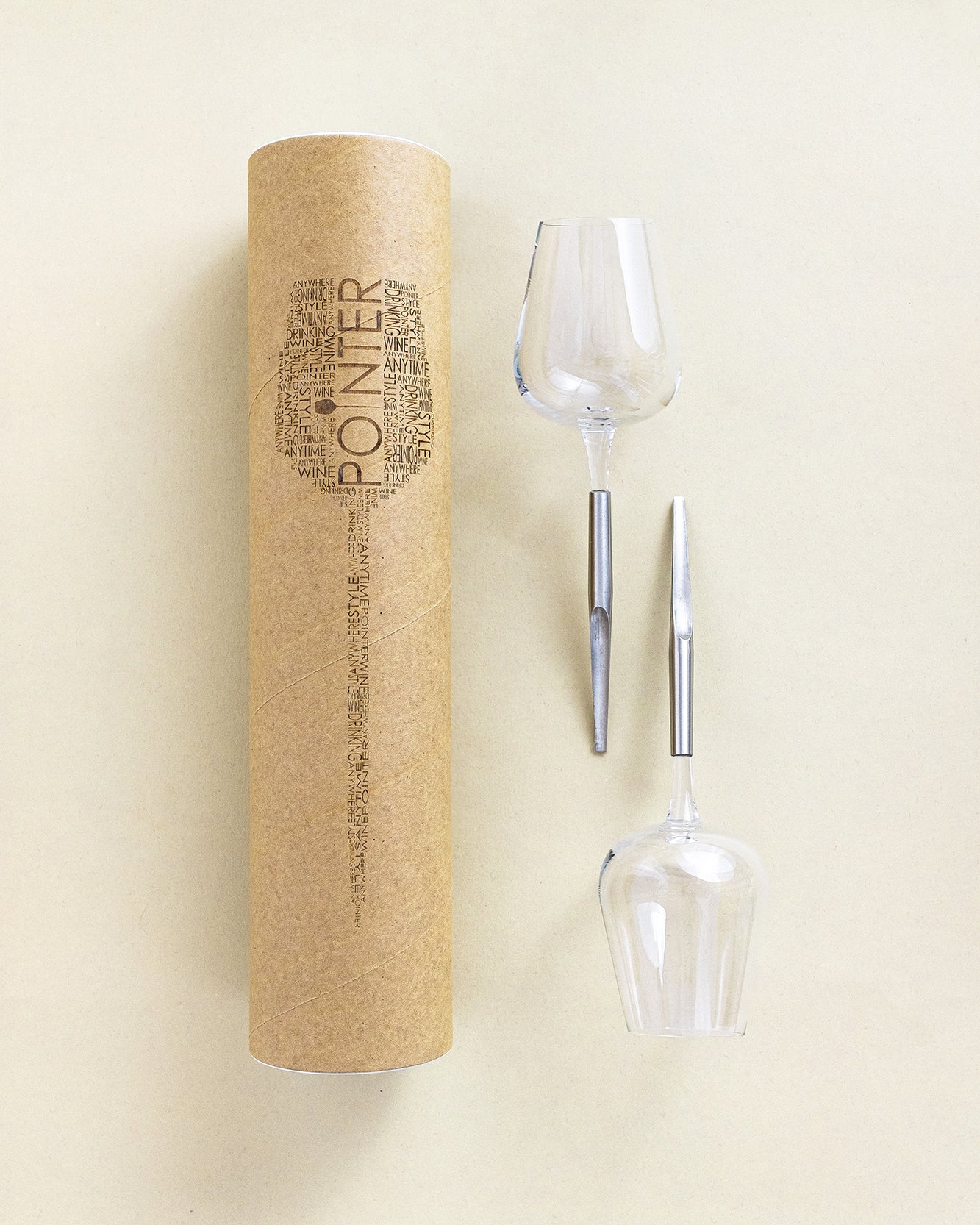 2 picnic wine glasses with metal pin placed horizontally next to their cardboard packing tube for transport